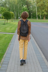 A person with a backpack is walking on the sidewalk. Vertical photo.