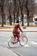 Naklejka na ściany i meble Young girl in a red autumn coat rides a bicycle on a crosswalk (949)