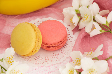 Fototapeta na wymiar two French macaroons, pink and yellow on a pink background with flowers and a banana. Banana and raspberry macaroon are close. Fragrant macaroons concept. High quality photo