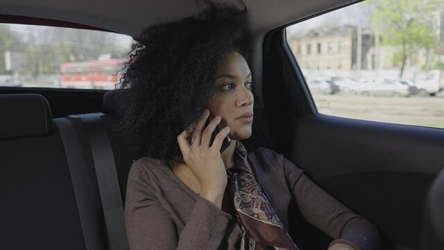 Portrait of stylish young African American woman talking on smartphone. A mixed race female riding in a car in the back seat. Close up. Slow motion ready 59.97fps.