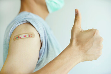 A man showing his arm get vaccinated with multicolor ' VACCINATED ' write on wound plaster and show thumb up feeling good and be strong                                               
