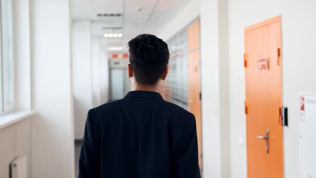 The guy walks along the narrow corridor of the office, holding a laptop. Young