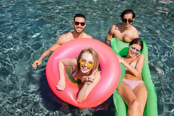 high angle view of young woman showing victory gesture near joyful interracial friends in swimming...