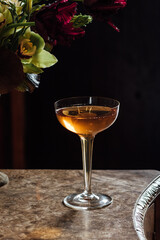 whiskey cocktail in champagne coupe glass with flowers in vase dark background