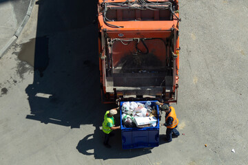 Garbage removal. The scavengers are rolling the trash can to the garbage truck, top view. Garbage loading process.