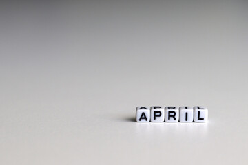 APRIL text on white cubic blocks. The letters are written on the cubes in black letters highlighted on the glass surface. APRIL, text for your design