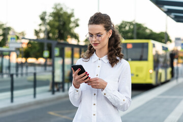 Fototapeta premium Young business woman using a mobile phone on the go in the city. Happy business woman using phone at railroad station.
