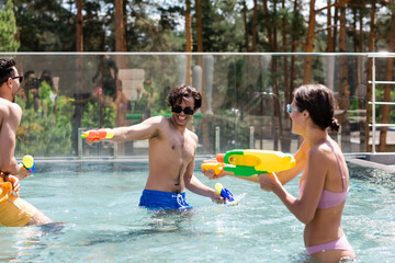 excited interracial friends playing water battle game in swimming pool