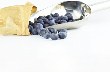 Blueberries in a metal spoon, next to kraft paper sack bag and scattered on the white background. Copy space.