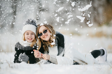 Front view of beautiful mother and her little adorable daughter lying on the snow. Concept of mother-daughter relationships.