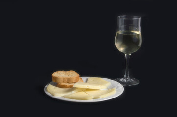 still life with plate with cheese and bread and a glass of white wine, isolated on black background