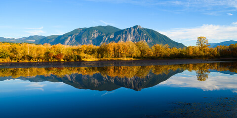 Fall colors reflect in the calm water of Borst Lake also known as Snoqualmie Mill Pond from its role in the former lumber yard.  Mount Si rises on a sunny blue sky day