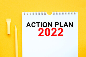 Notebook, pen and words ACTION PLAN 2022 on yellow