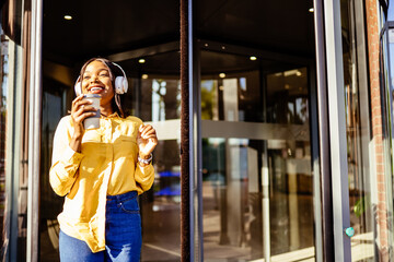 Loving african girl singing and dancing while to leave the modern. building. Outdoor portrait of happy smiling young black woman in headphones enjoying favorite song.