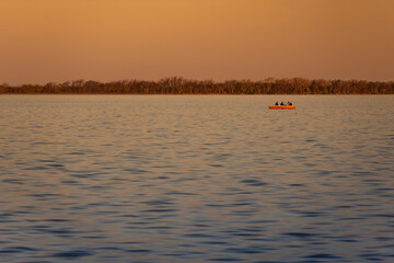 Fishers in a little boat in Lobos Lagoon, Buenos Aires, Argentina. Photo taken at sunset with a rare orange sky reflacting over the water. 