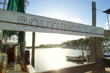 A weathered Southport , NC sign hangs at a dock in front of a fishing boat on the Cape Fear River