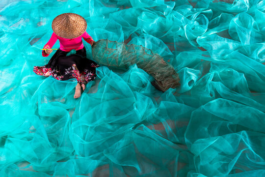 China Fujian Province Xiapu Zhujiang Island. A woman sews and mends fishing gear on a colorful turquoise net.