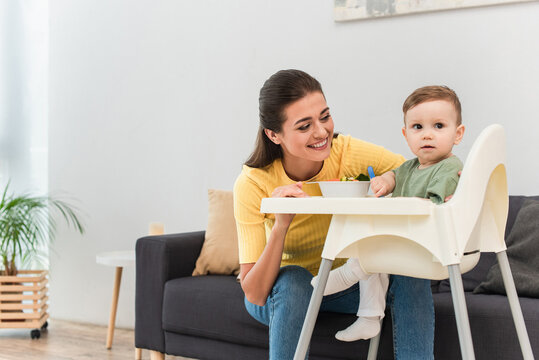 Happy Mother Looking At Kid Near Food On High Chair