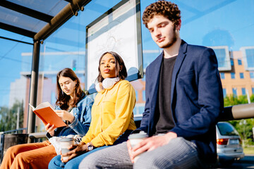 Three youth people young man and women waiting at the bus stop. Millennials passengers traveling with public transport concept. © Iryna