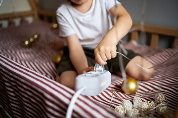 Child safety at home concept. The child inserts a plug into the socket to turn on the New Year's...