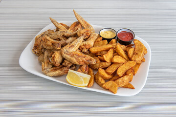 Large portion of olive oil fried wings garnished with fancy fries, lemon for garnish and ketchup and mustard for dipping