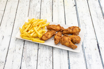 tray of fried wings battered in flour garnished with French fries on a white table
