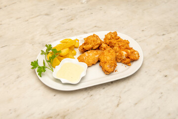 Tray of chicken wings battered with egg and flour and spicy flavor with dipping sauce garnished with French fries and parsley