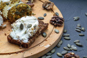 white soft cheese is spread on black bread and sprinkled with pumpkin seeds. peach bread and cheese