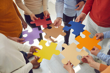 Team of multiethnic business people and colleagues join colorful jigsaw puzzle pieces as metaphor for teamwork, creative search and looking for solutions together