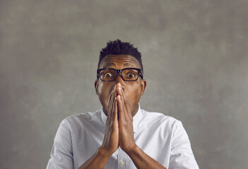 Afraid scared african american man covering mouth with hands feel horrified portrait. Studio shot of stunned emotional young black guy received shocking news looking at camera on grey copy space