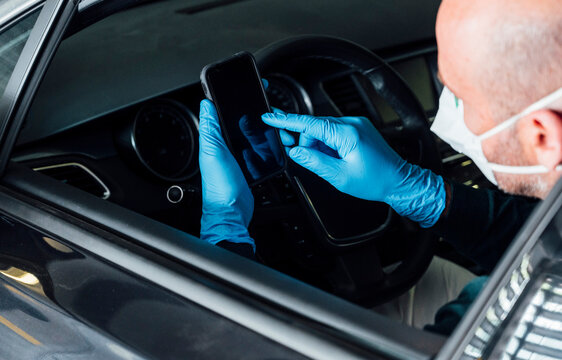 Bald man with protective mask inside a car browsing on smartphone