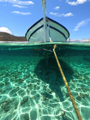 Sea level and underwater split photo of traditional wooden fishing boat anchored in Aegean island port with emerald crystal clear sea