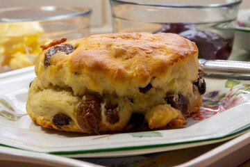 Freshly Baked Fruit Scone on a side plate with Butter and Jam in the background
