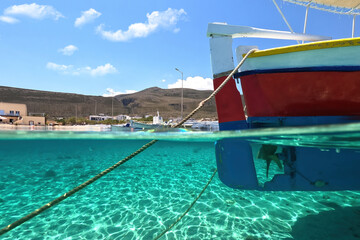Fototapeta na wymiar Sea level and underwater split photo of traditional wooden fishing boat anchored in Aegean island port with emerald crystal clear sea