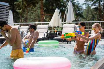 excited women fighting on water guns near multiethnic friends in swimming pool