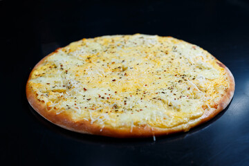 Delicious Four Cheeses pizza with cheddar, parmesan, mozzarella and tomato sauce on a black background. View from above.