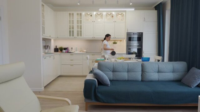 Housewife doing household chores, woman cleaning kitchen, modern white apartment interior with open floor plan. High quality 4k footage