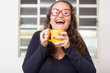 Mulher feliz usando óculos vermelhos e segurando uma caneca amarela.