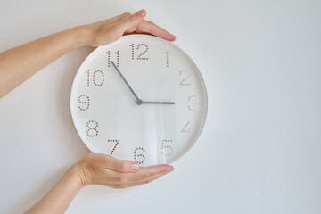 The girl is holding a white round wall clock hanging on the wall. A minimalistic image of a wall...