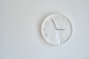 White round wall clock hanging on the wall. A minimalistic image of a wall clock on a white...