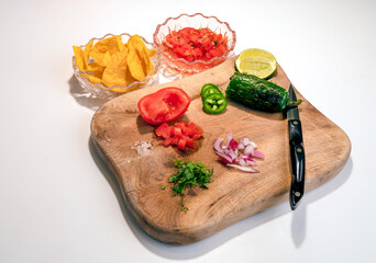 Chips and salsa ingredients on a wood cutting board with a snap knife on a white background with copy space.