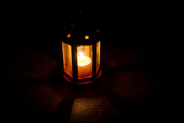 Spooky candle lamp with star shaped holes shining from inside. Lighting dimly the floor and projecting shadows