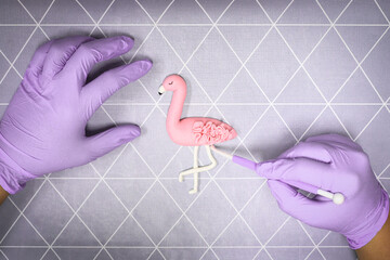 Close up photography of hands using  modeling tool to create fondant flamingo. Rose and purple...