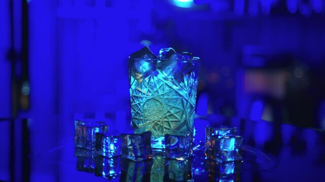 Bartender sets fire to alcohol cocktail, blue background. Flames in cocktail glass in slow motion, burning ice in alcohol drink, barman makes drink.