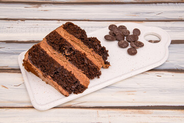 Portion of chocolate cake with three layers of biscuits and filling with chocolate chips on one side on white table