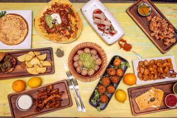 Image of a set of dishes of mainly Spanish food with touches of Mexican cuisine. Wrinkled potatoes with mojo, patatas bravas, nachos with guacamole, potato omelette, belly salad