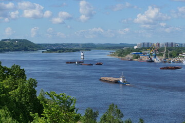 Nice view of the river. A tugboat with a barge loaded with wooden logs is sailing along the river....