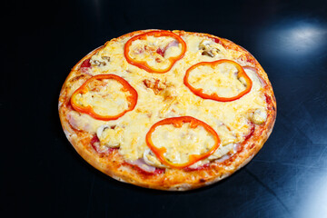 Hot delicious homemade American pizza with red pepper and meat with a thick crust on a black table