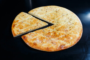 Sliced pizza on a black stone background, top view. Freshly baked focaccia with cheese