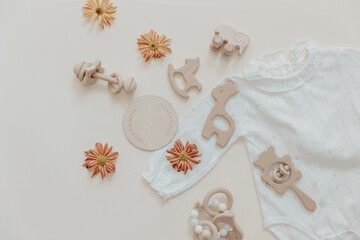 Clothes for baby and newborns: white bodysuits and accessories neutral beige and brown colors. Eco friendly wooden toys on Light background, top view, flat lay.